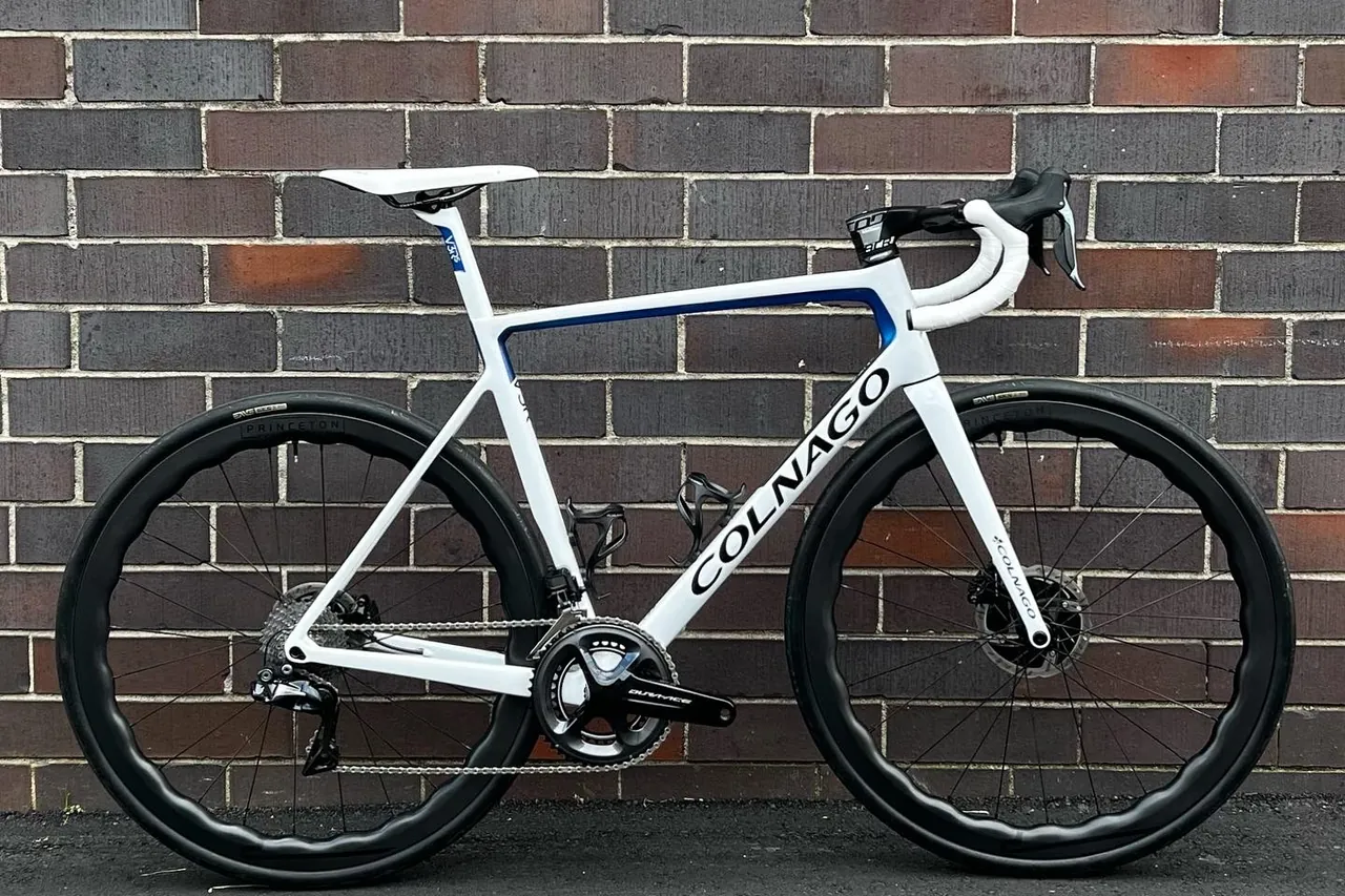 White Colnago V3-RS road bike with blue details and deep carbon wheels against a brick wall