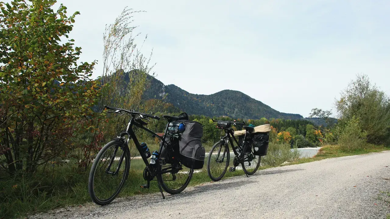 Two touring bikes with panniers parked on a gravel path below wooded mountains