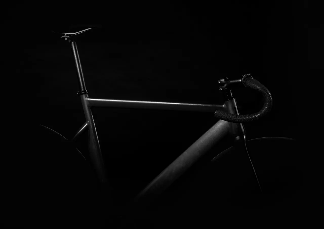 Black-and-white study of a bicycle frame and handlebar against a black background
