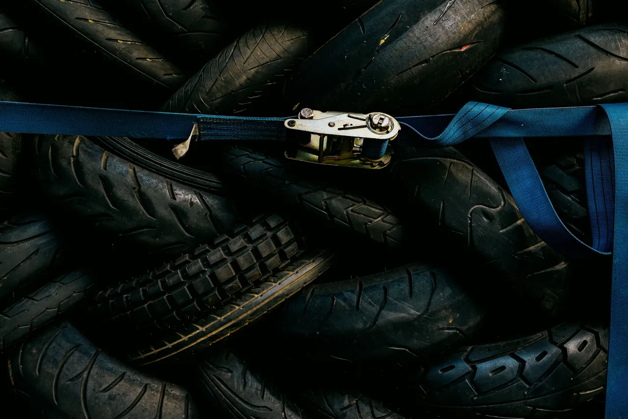 Pile of used rubber tyres held together with a blue ratchet strap